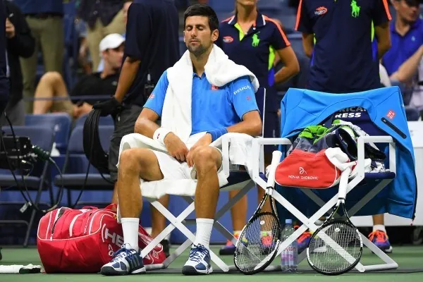 Novak Djokovic sitting on the bench, eyes closed.